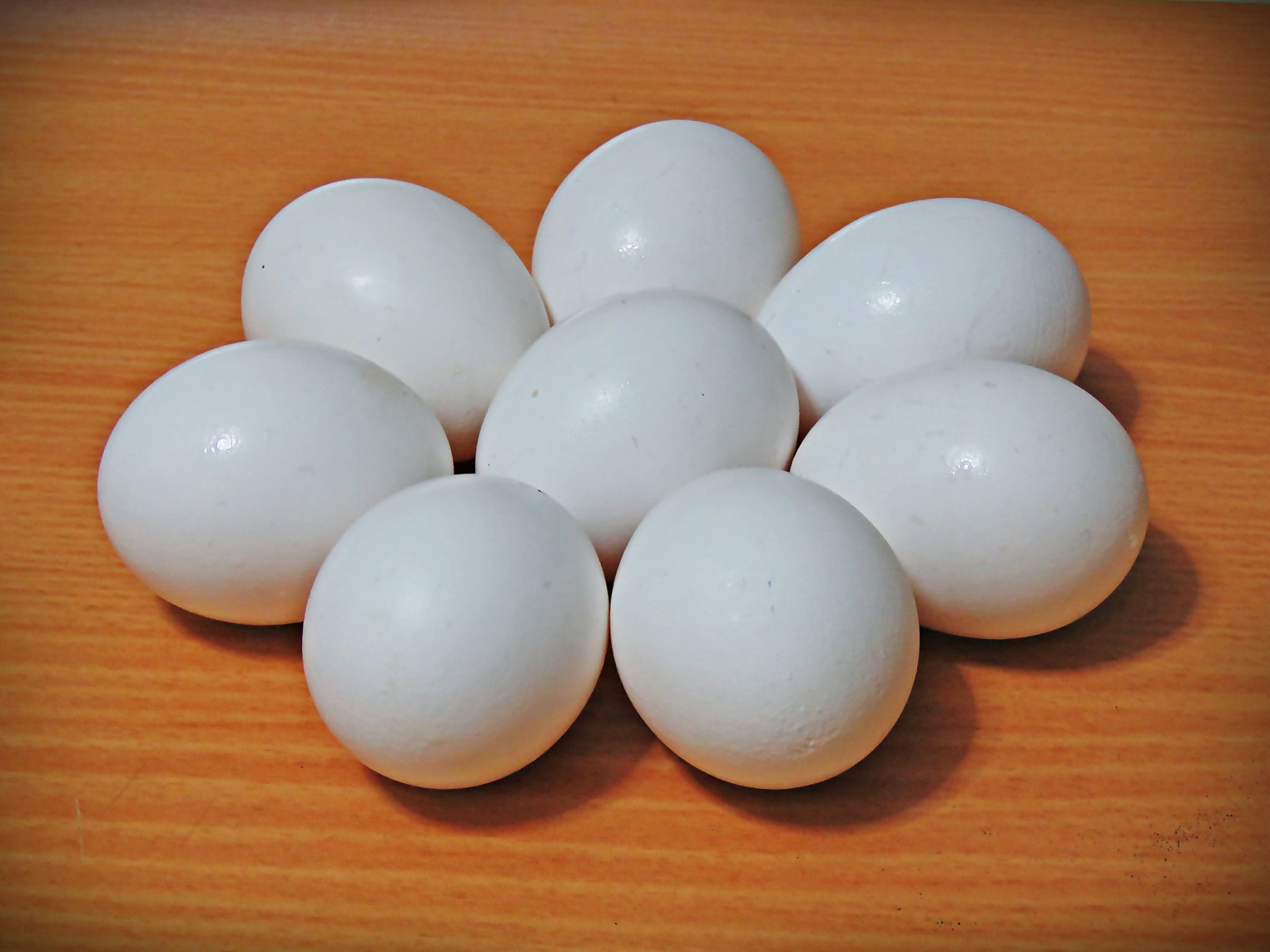 Eight white eggs are arranged in a flower-like pattern on a light brown wooden surface.