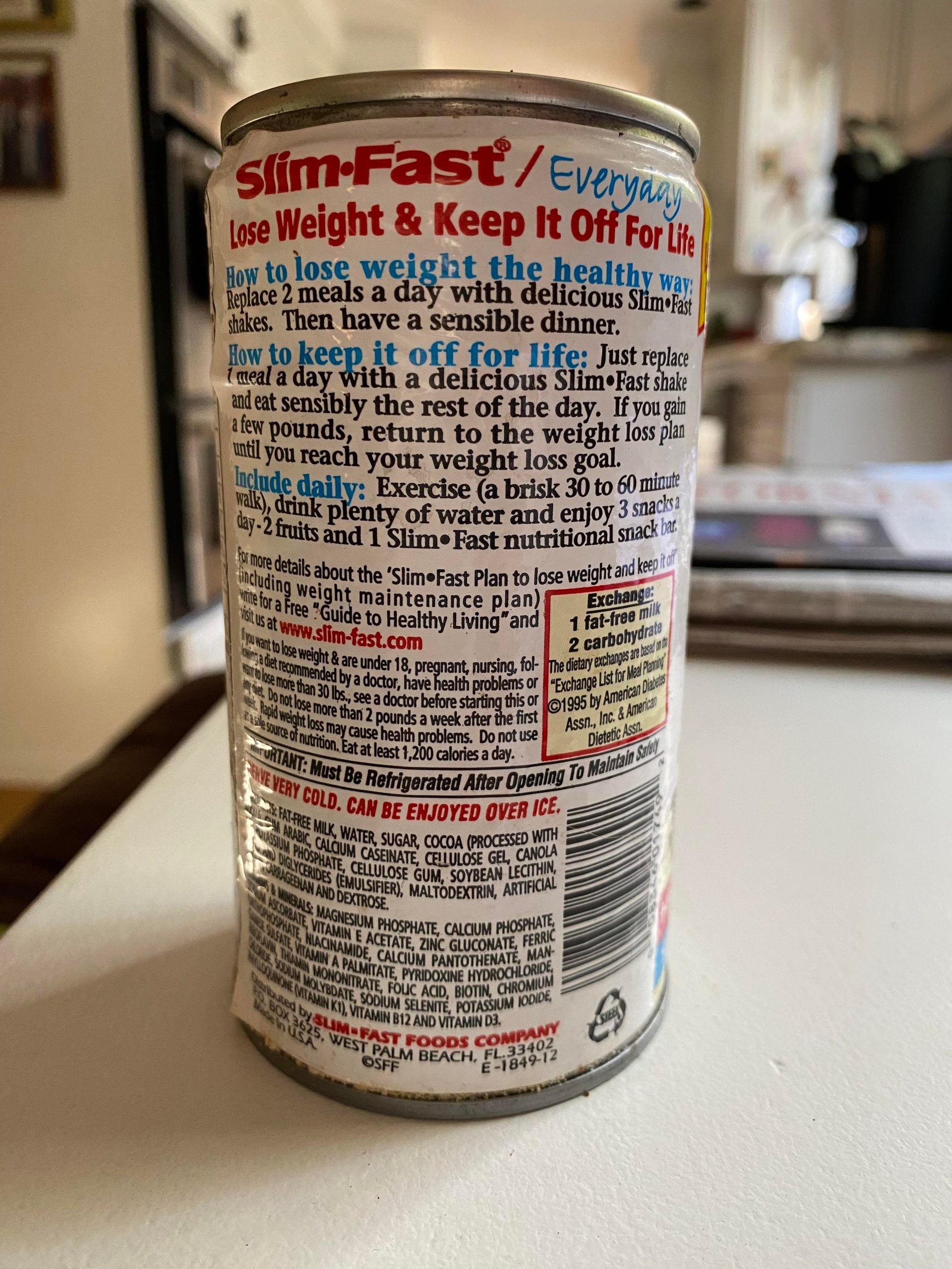 A can of Slim-Fast with colorful text describing how to use the meal replacement for weight loss and maintenance, nutrition facts, and instructions printed on the back label, sitting on a kitchen counter.