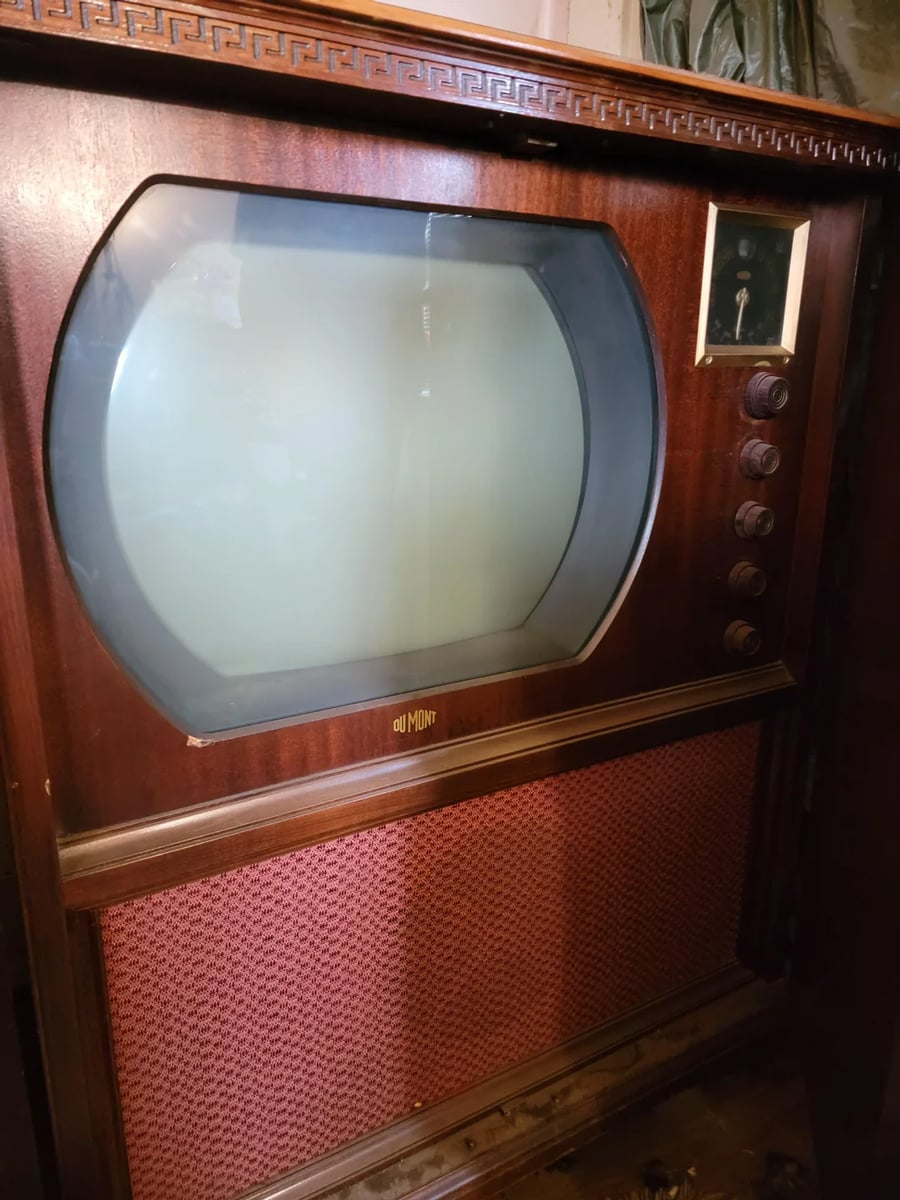 A vintage wooden console television with a large rounded screen, control knobs on the right, and a mesh speaker cover below. The brand name “Du Mont” is visible on the front.