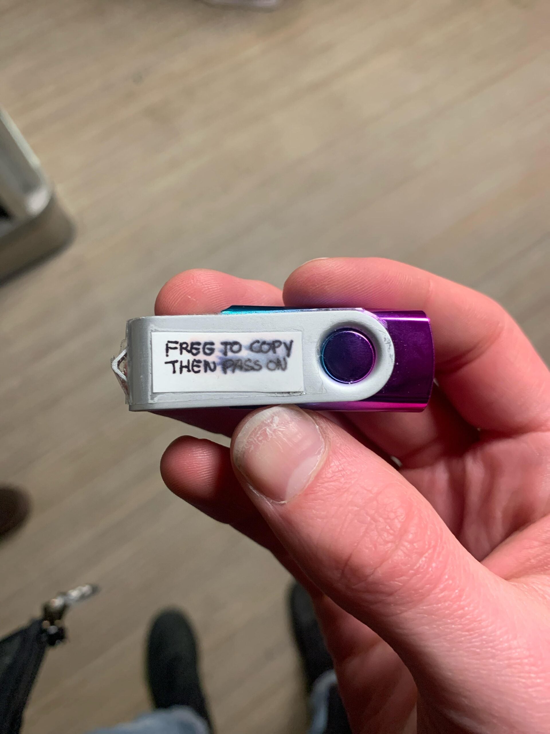 A hand holding a purple and silver USB flash drive labeled “FREE TO COPY THEN PASS ON” written in pen on white tape.