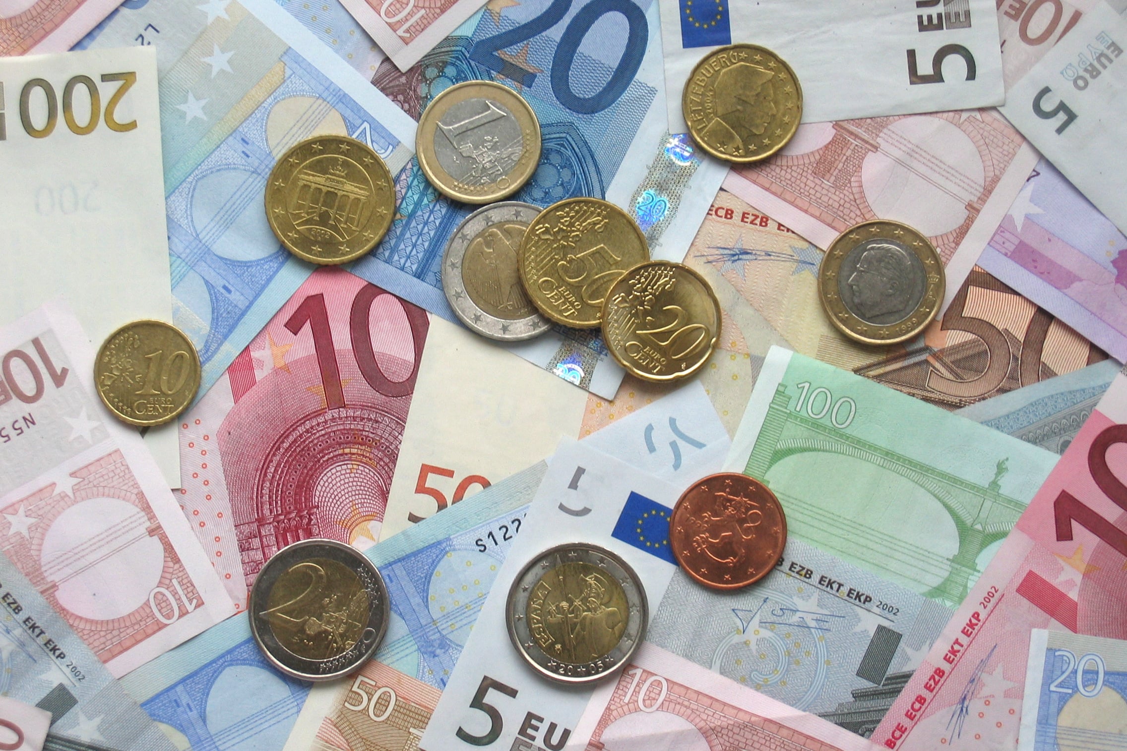 Various euro banknotes and coins are scattered, including denominations of 5, 10, 20, 50, 100, and 200 euro notes, and several euro coins in different values.