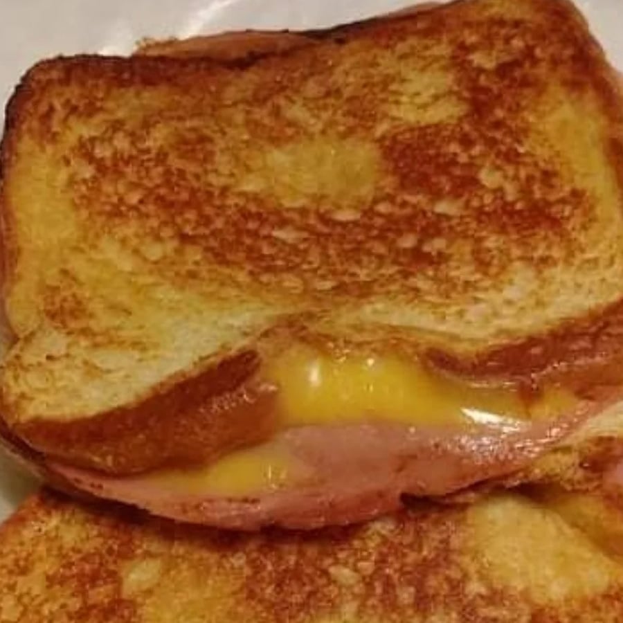 A close-up of a grilled sandwich with melted cheese and a slice of ham between two pieces of toasted bread.