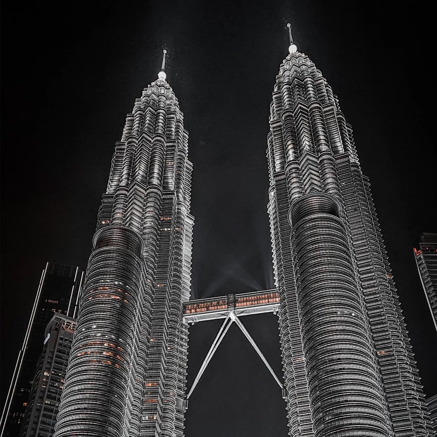 The image shows the illuminated Petronas Twin Towers at night in Kuala Lumpur, Malaysia, with the skybridge connecting the two skyscrapers.