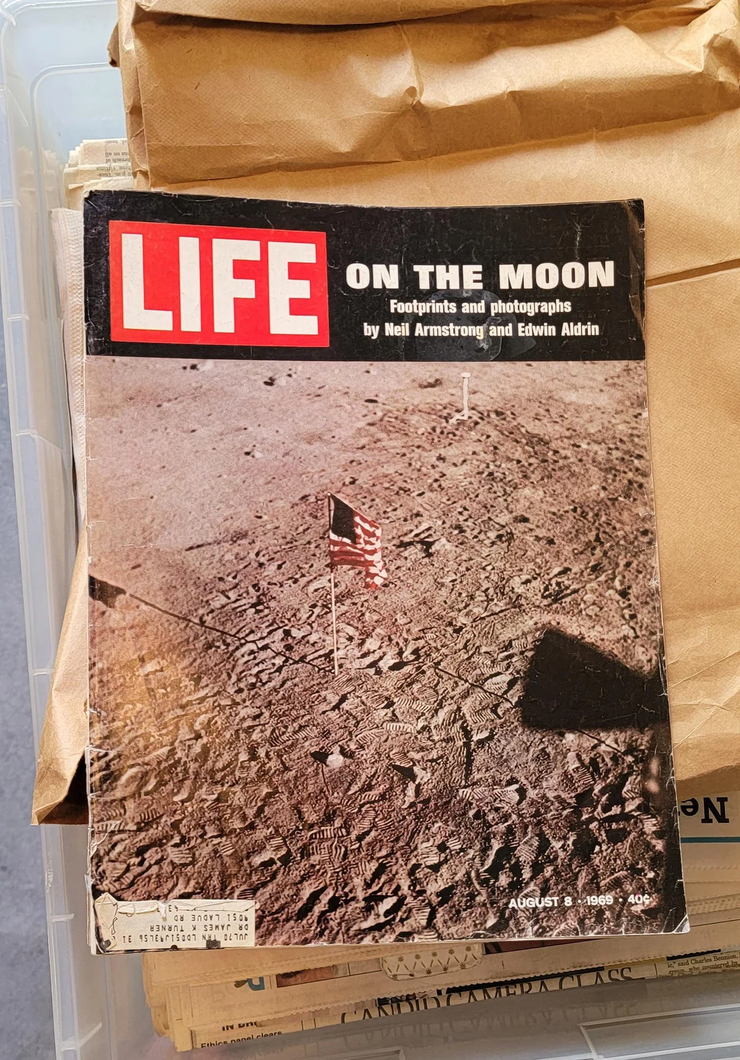 A LIFE magazine cover titled “ON THE MOON” with a photo of the lunar surface, a U.S. flag, and astronaut footprints. Dated August 1969.