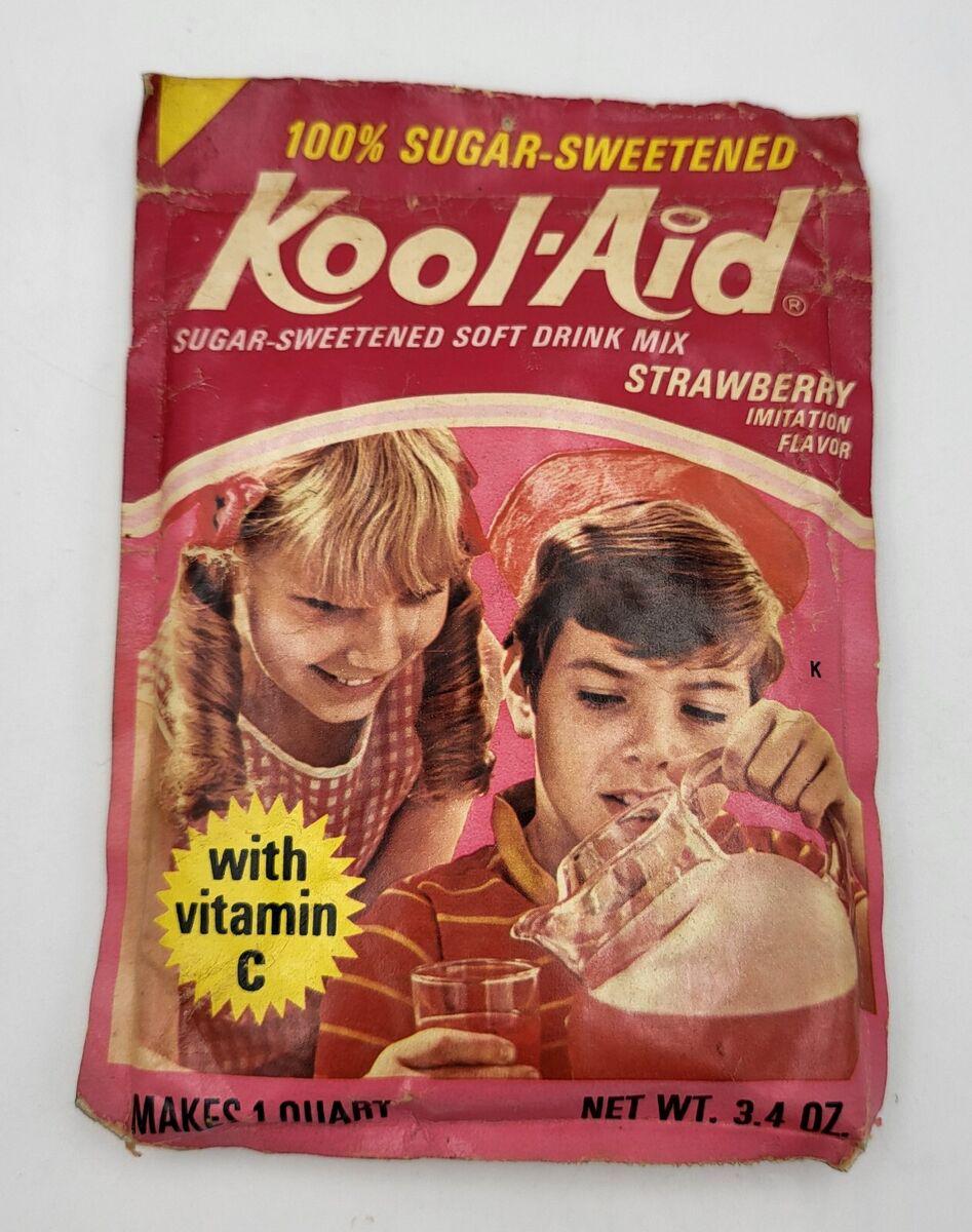 A vintage Kool-Aid packet, strawberry flavor, shows a girl and boy smiling as the boy pours Kool-Aid into a glass. The packet advertises “100% sugar-sweetened” and “with vitamin C.” Bright pink and yellow design.
