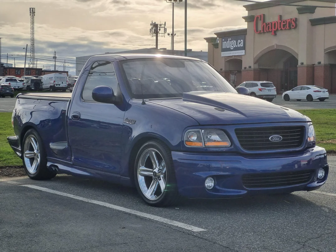 A blue Ford pickup truck is parked in a lot near a Chapters store, with other cars and buildings visible in the background.