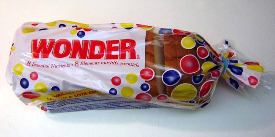 A loaf of Wonder Bread in a white plastic bag with red, yellow, and blue dots, labeled “Wonder” and “8 Essential Nutrients.”