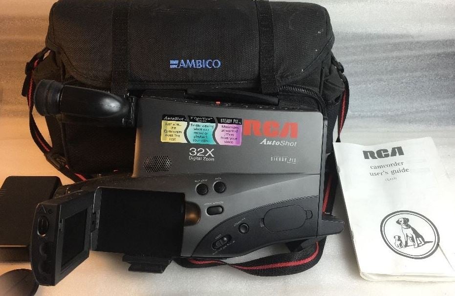 An RCA camcorder with a flip-out screen sits in front of a black Ambico bag and an RCA camcorder user’s guide, with brightly colored sticky notes on the camera.