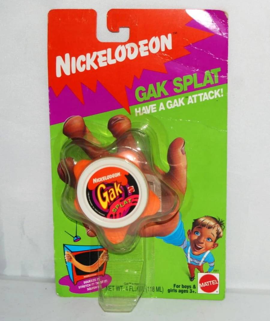 Nickelodeon Gak Splat toy in original packaging, featuring bright colors, hand-shaped orange slime, and cartoon graphics. Text says “Have a Gak Attack!” For boys and girls ages 3+.