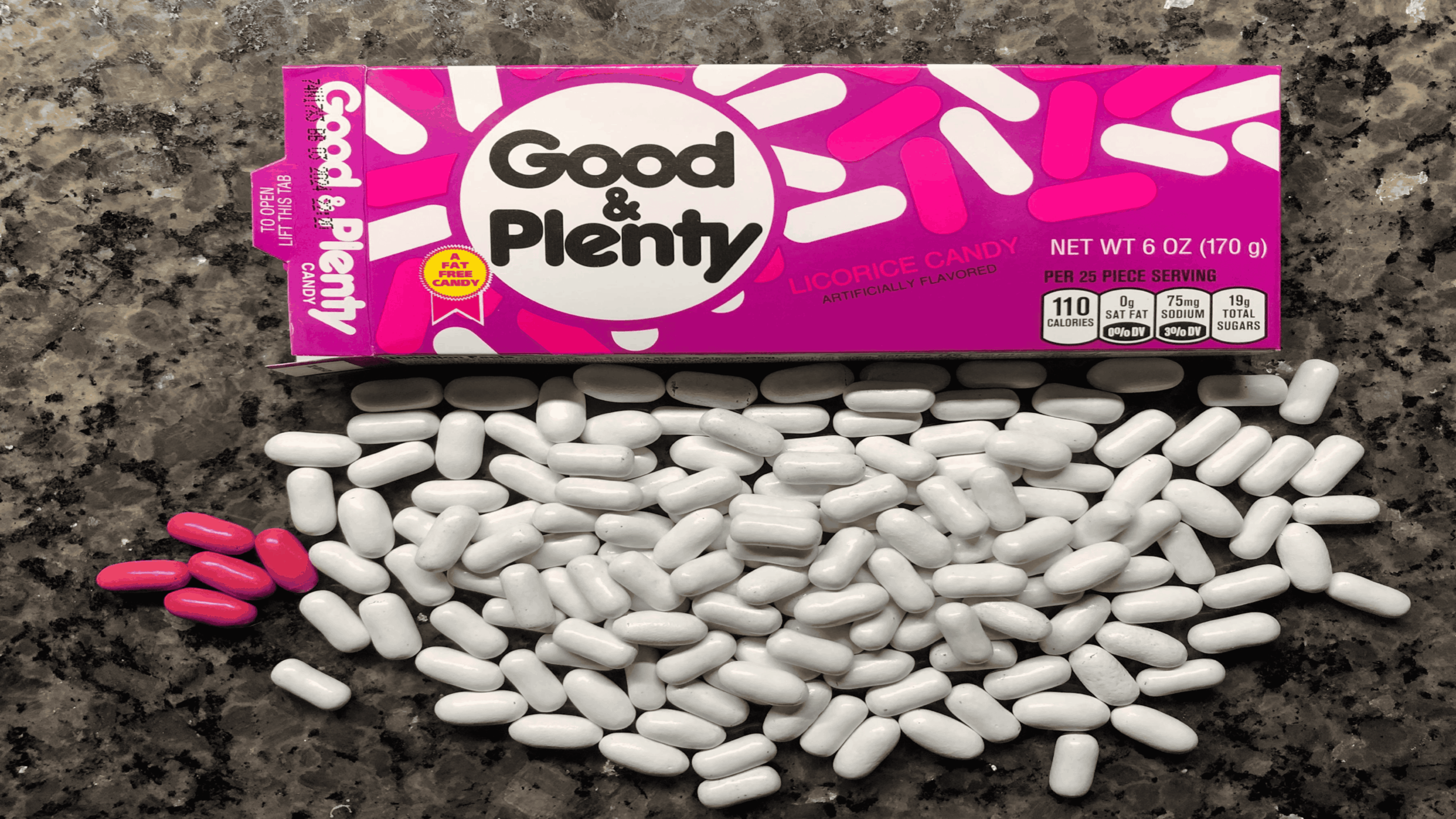 A box of Good & Plenty licorice candy is open on a speckled countertop, with many white and a few pink candy pieces spilled out in front of it.