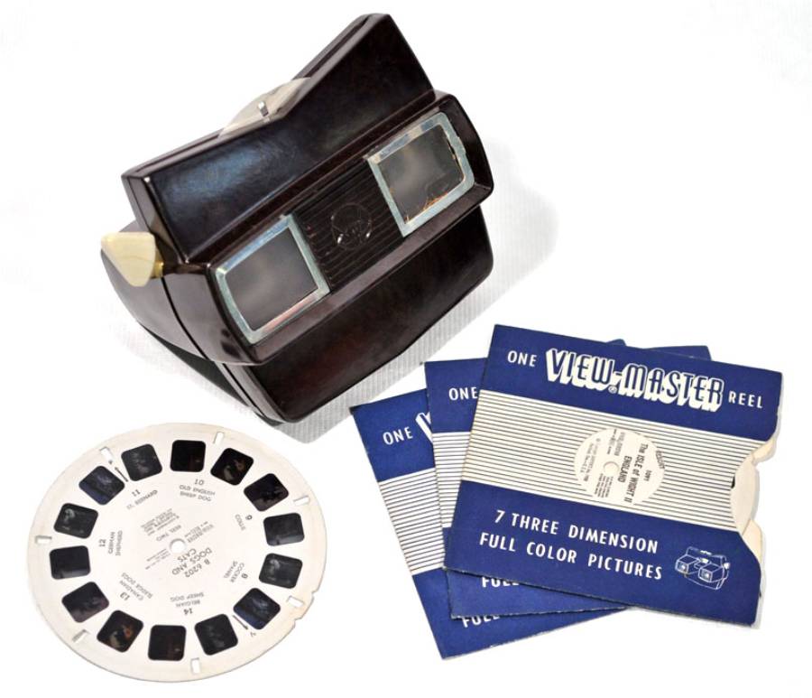 A vintage View-Master viewer, a round photo reel, and three blue View-Master reel packets labeled “7 three dimension full color pictures” are displayed on a white surface.