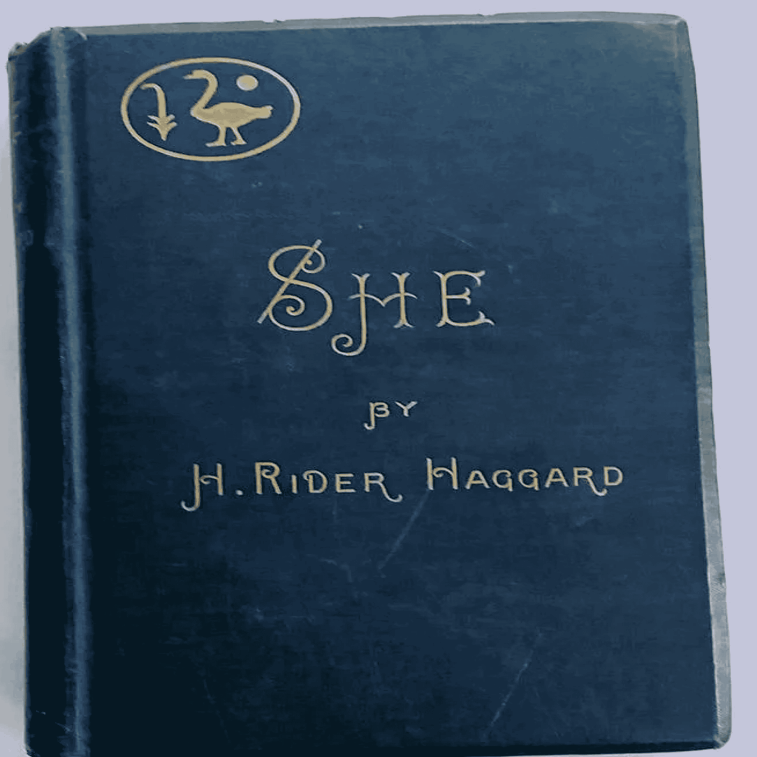 A dark blue book cover of “She” by H. Rider Haggard, featuring gold embossed text and a circular emblem with a bird and a staff in the top left corner.