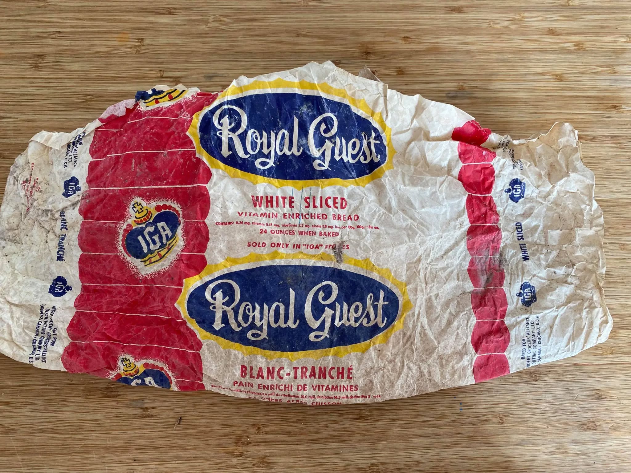 Crumpled Royal Guest bread wrapper with red, white, and blue design, displaying “White Sliced” and “Vitamin Enriched Bread” in English and French on a wooden surface.