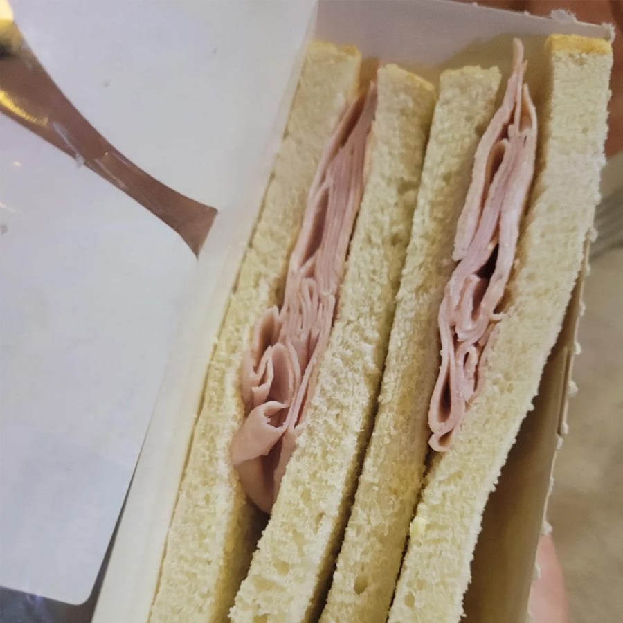 Two plain white bread sandwiches with thin slices of deli meat inside, placed side by side in a white cardboard container.