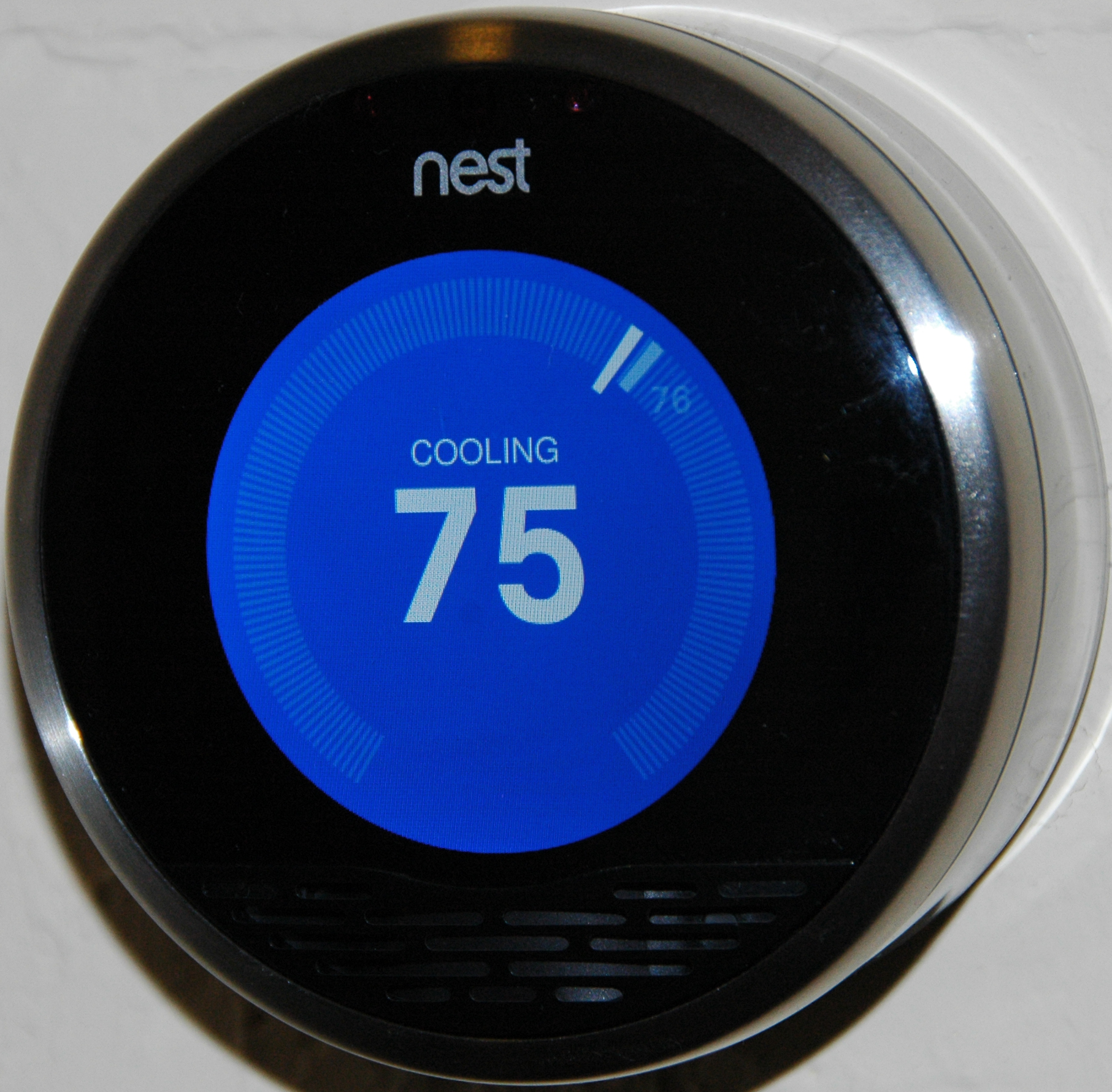 A Nest smart thermostat displays a blue screen reading “COOLING 75,” indicating the current cooling temperature setting.