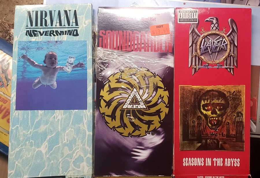 Three cassette tapes side by side: Nirvana’s “Nevermind” with a swimming baby cover, Soundgarden’s “Badmotorfinger” with a spinning gear, and Slayer’s “Seasons in the Abyss” featuring a dark skull artwork.