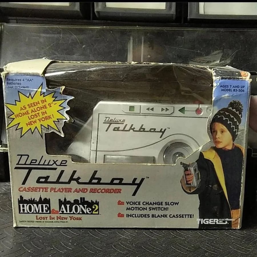 A Deluxe Talkboy cassette player and recorder in its box, featuring a child holding the device and a promo for “Home Alone 2: Lost in New York.” The box highlights its features and age recommendation.