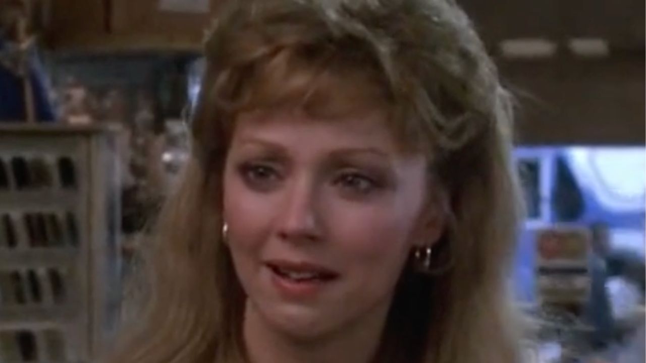 A woman with wavy blonde hair and hoop earrings looks emotional and teary-eyed while standing indoors, possibly in a store or shop.