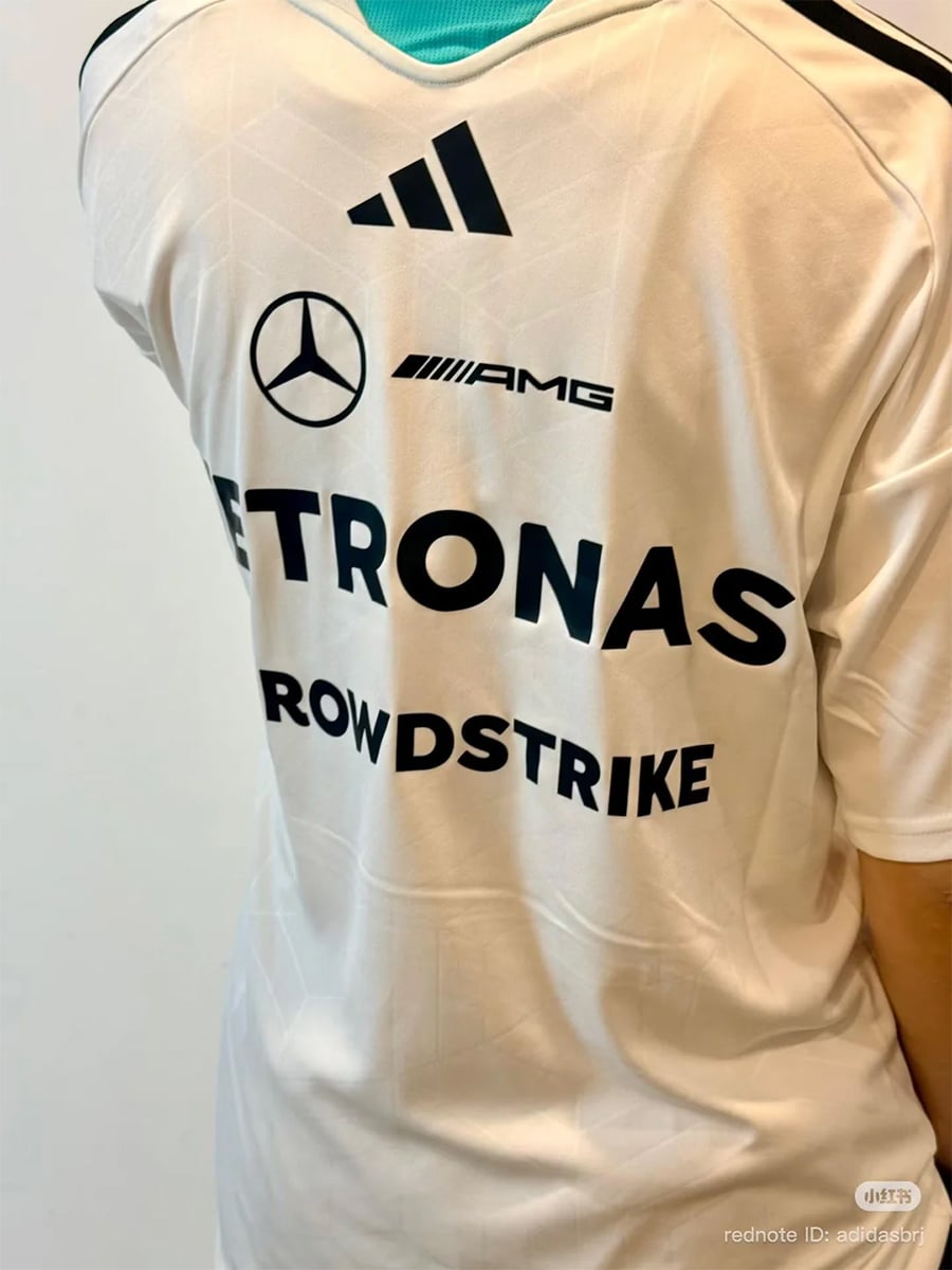 A person wearing a white sports jersey with black logos and text, including Mercedes, AMG, PETRONAS, and CrowdStrike, is shown from the back, slightly turned to the side.
