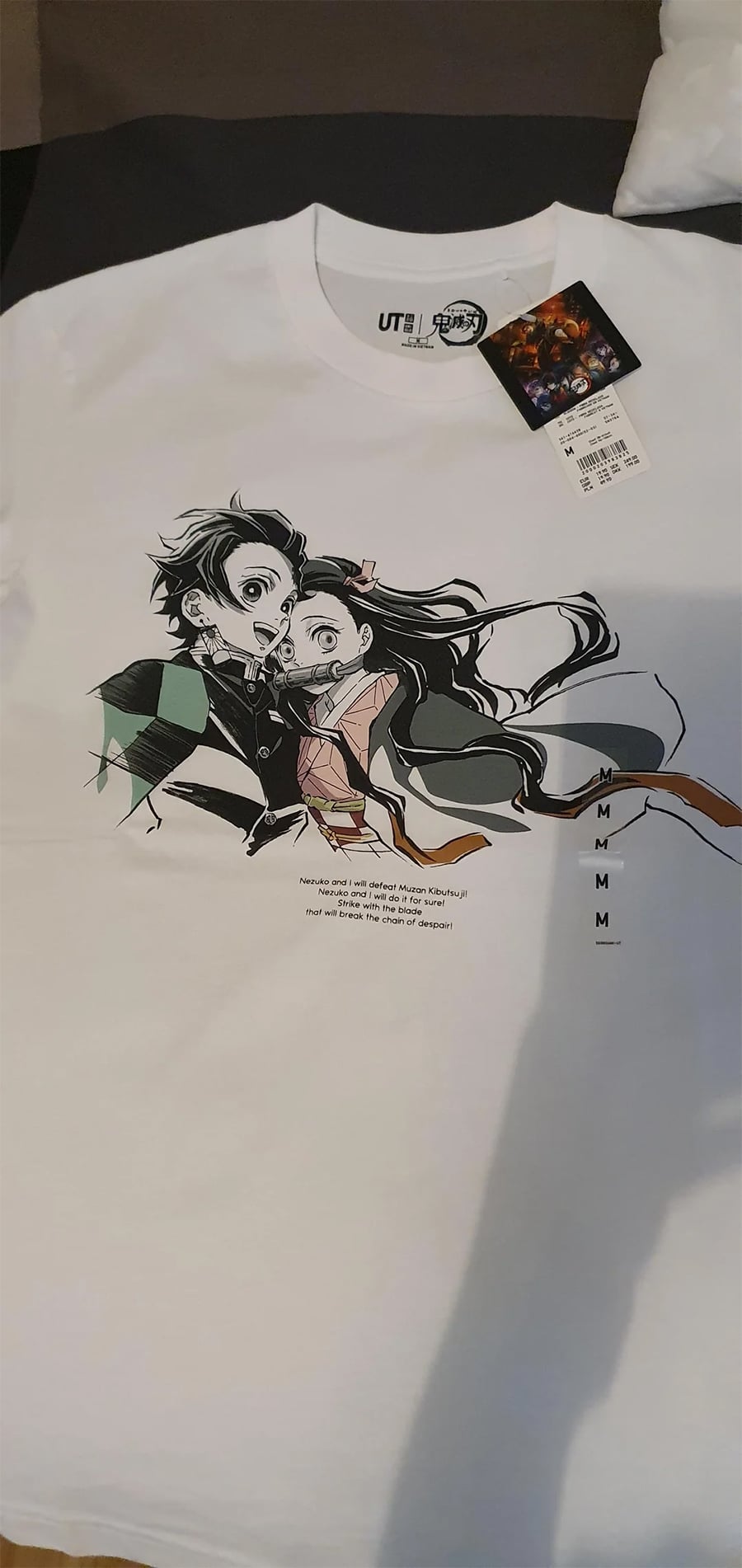 White T-shirt featuring Tanjiro and Nezuko from Demon Slayer, with a UT x Demon Slayer tag attached. The characters are illustrated in color, and there is a vertical text design next to them.