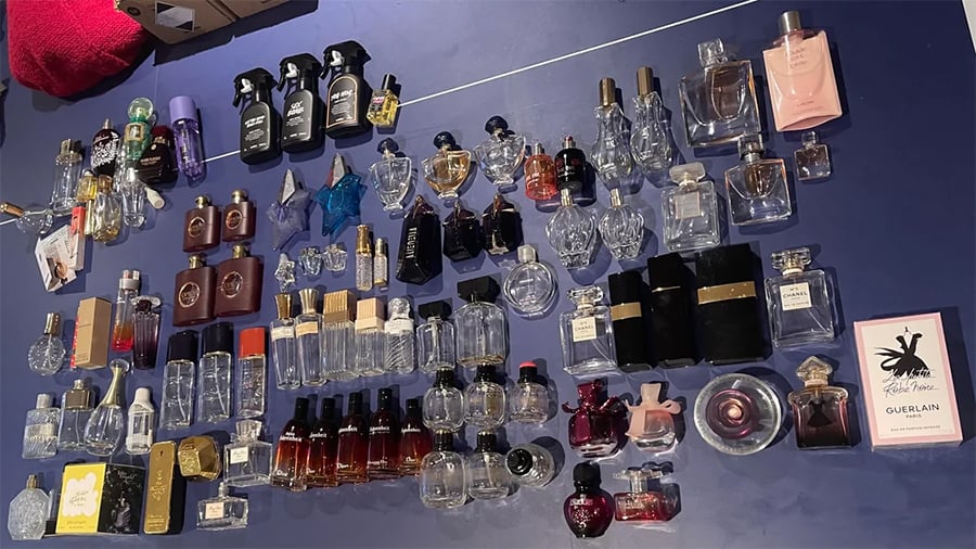 A large collection of assorted perfume bottles, some clear and some colored, is arranged on a blue surface. Bottles vary in size, shape, and brand, with some boxes and packaging also visible.