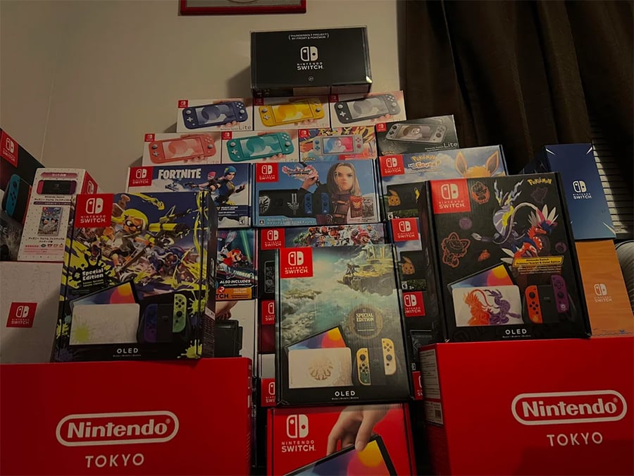 A large collection of Nintendo Switch OLED consoles, special editions, accessories, and Nintendo Tokyo shopping bags stacked in a dimly lit room.