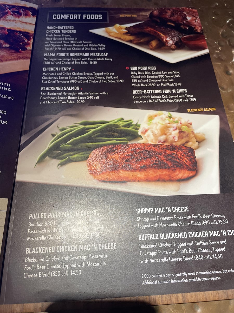 Menu section titled “Comfort Foods” showing food options and prices. Featured is a plate with blackened salmon, green beans, and mashed potatoes. The menu includes descriptions of several dishes and sides.
