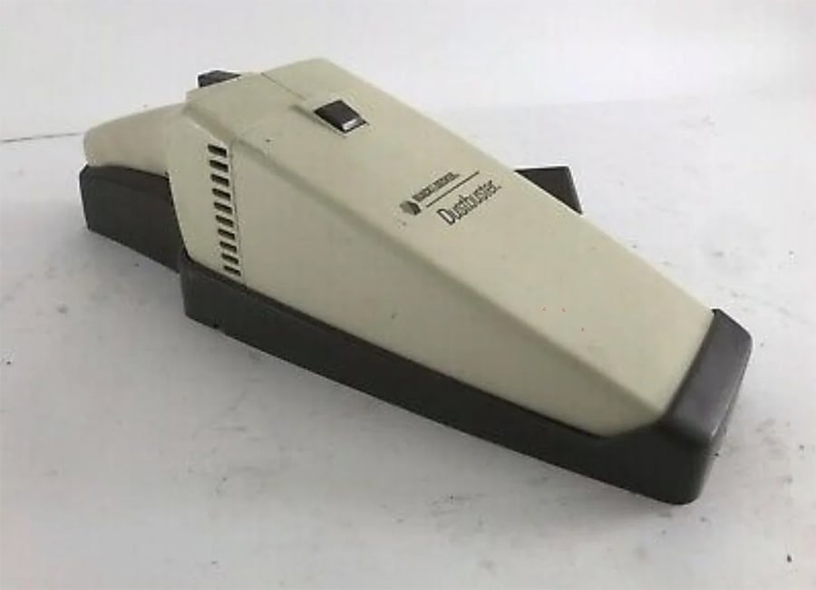 A beige and black handheld DustBuster vacuum cleaner sits on a white surface, with a simple, rectangular design and a power switch on top.