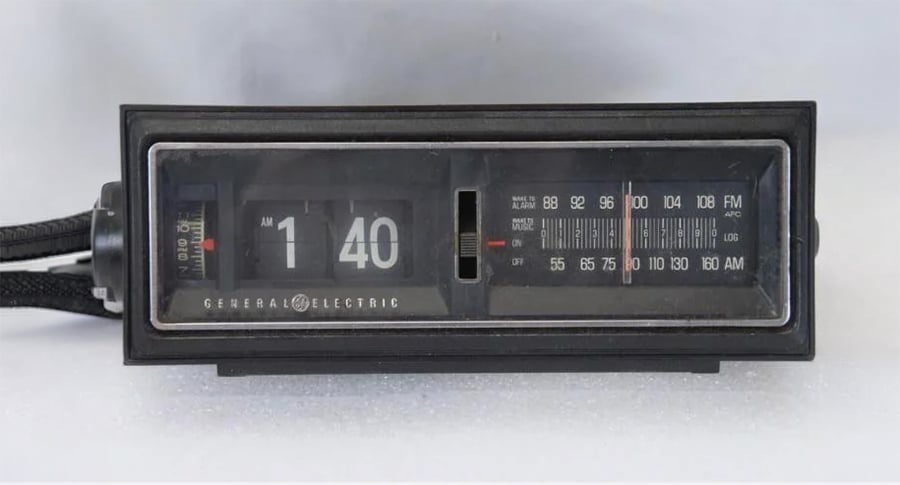 A vintage General Electric flip clock radio displays the time as 1:40. The device features a black casing with both AM and FM radio dials on the right side.