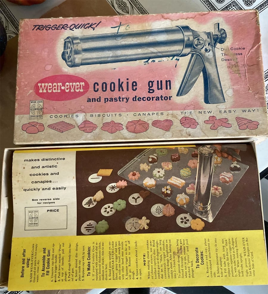 Vintage Wear-Ever cookie gun and pastry decorator box, partially open, showing the metal cookie gun, various decorative discs, and colorful cookies on a tray. Box has pink and yellow design and product details.