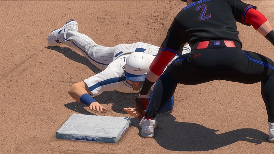 A baseball player in white slides headfirst toward a base as an opposing player in black attempts to tag him with a glove. Both players are on a dirt field.