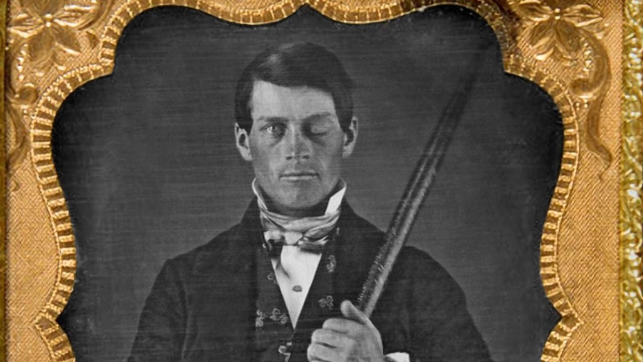 A black-and-white portrait of a man in 19th-century attire holding a metal rod, with a damaged left eye. The ornate gold frame decorates the top of the image.