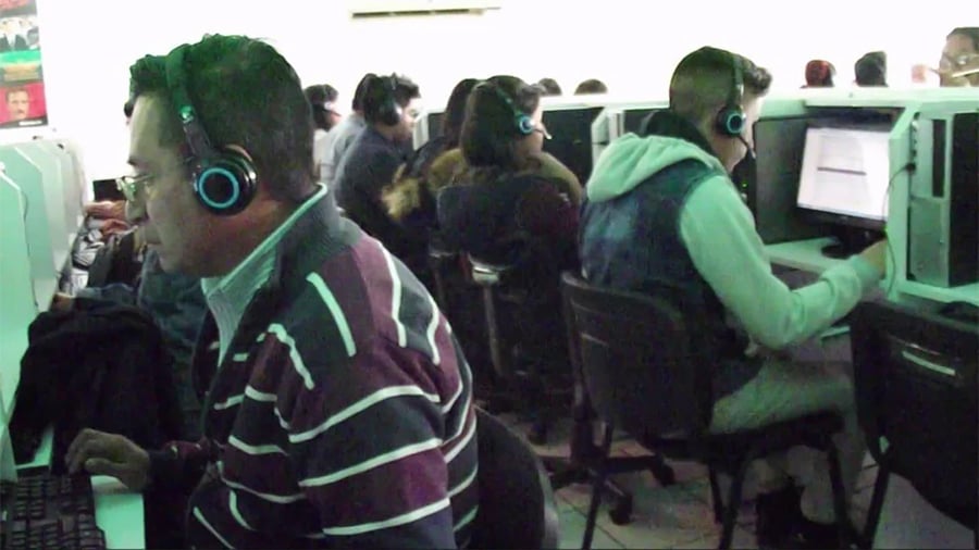 Several people wearing headsets work at computers in a call center. They sit at desks separated by partitions, focusing on their screens in a brightly lit room.
