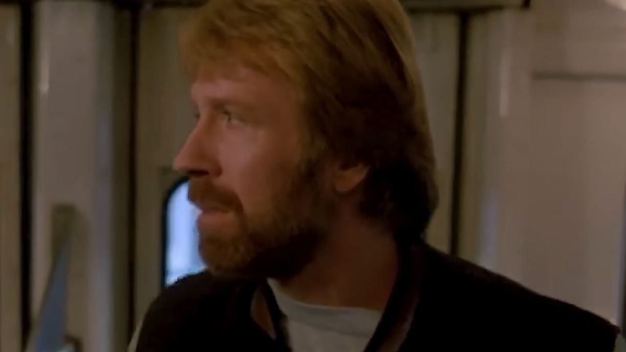 A man with light brown hair and a beard looks to his left inside a room with light-colored walls and a window in the background.