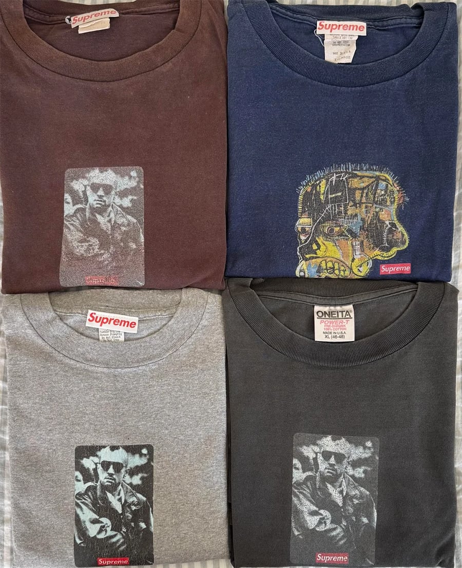 Four folded Supreme t-shirts are displayed. Three have a black-and-white graphic of a person wearing sunglasses and a jacket, while one has a graphic face with various colors. Each shirt’s Supreme tag is visible.