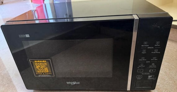 A black Whirlpool microwave oven with a digital control panel and a QR code sticker on the door, placed on a countertop.