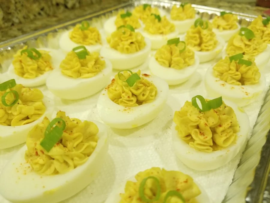 Tray of deviled eggs, each topped with a swirl of yellow filling and garnished with sliced green onions. The eggs are arranged neatly on a white paper towel.