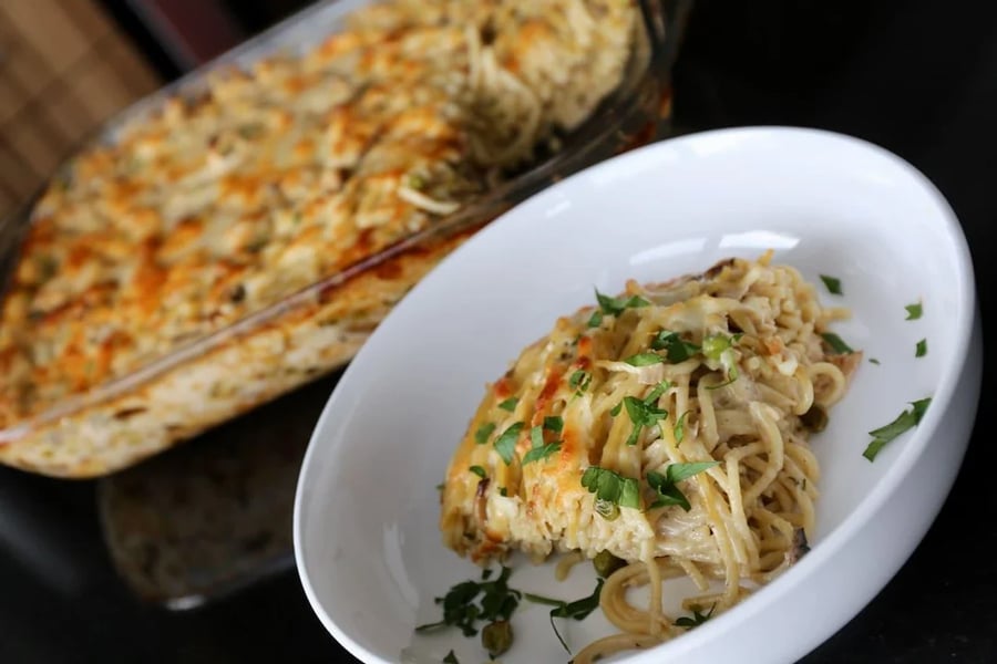 A serving of baked spaghetti with melted cheese and herbs on top, plated in a white bowl, with the baking dish in the background.