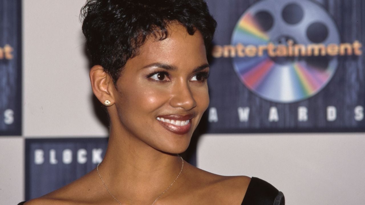 A woman with short curly hair and a black dress smiles at an event, standing in front of a backdrop featuring a film reel graphic and the words “Entertainment Awards.”