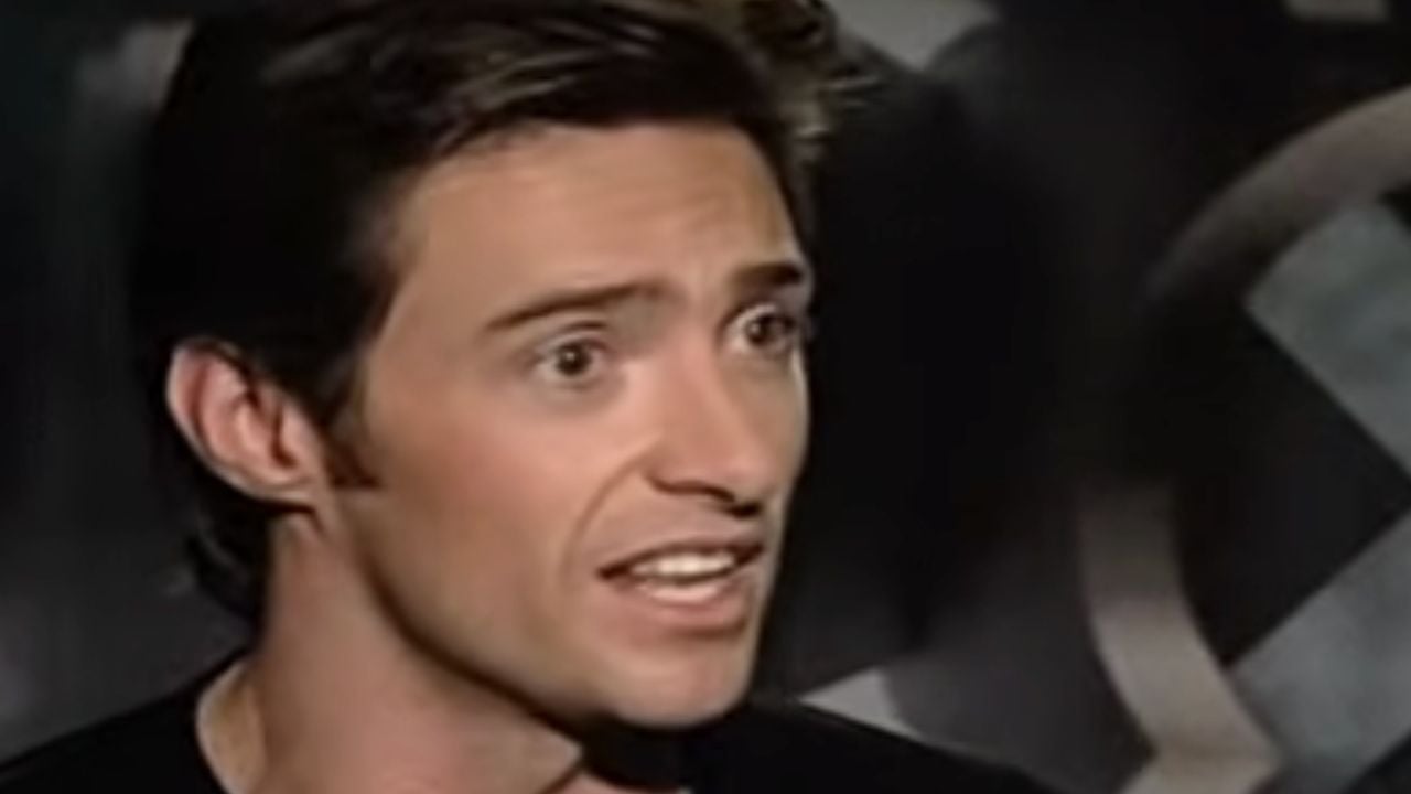 A man with dark hair speaks animatedly, looking slightly to the side. He is indoors, and the background is blurred with a circular pattern visible.