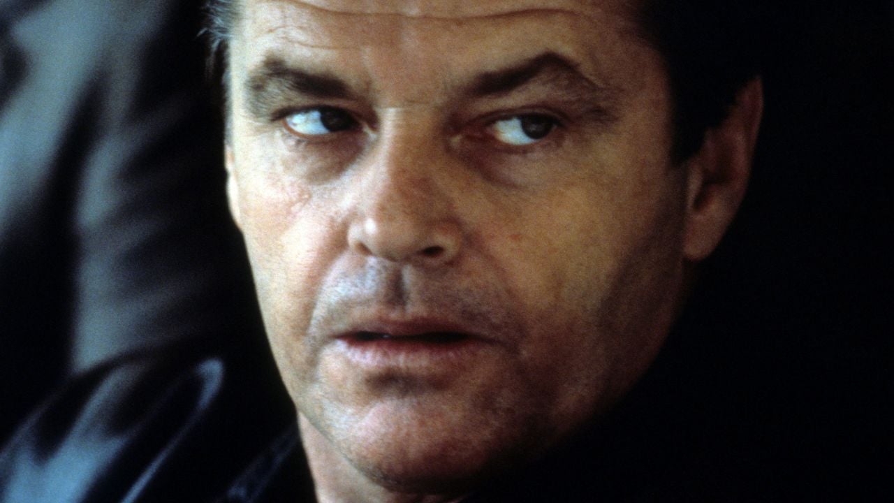 A close-up of a man with short hair and a serious expression, looking to his left. He is wearing a dark jacket and the background is out of focus.