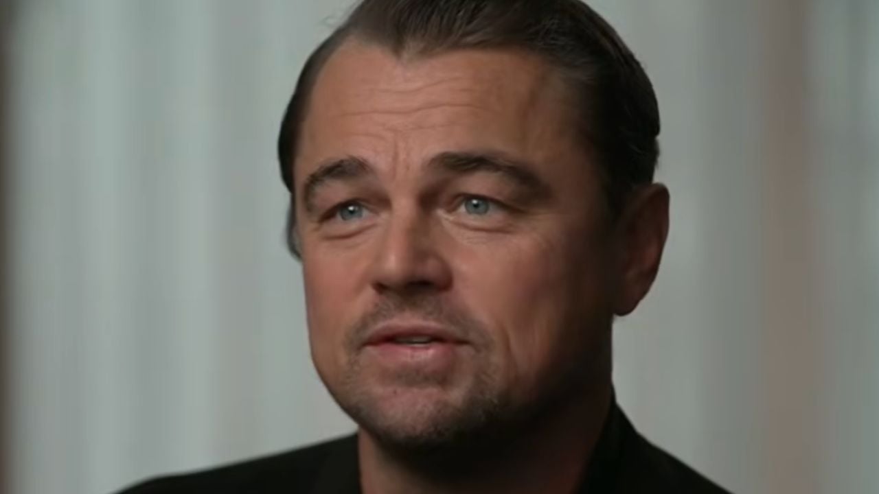 A man with slicked-back brown hair, blue eyes, and a trimmed beard is looking slightly off camera with a neutral expression. He is indoors, in front of a softly lit, neutral background.