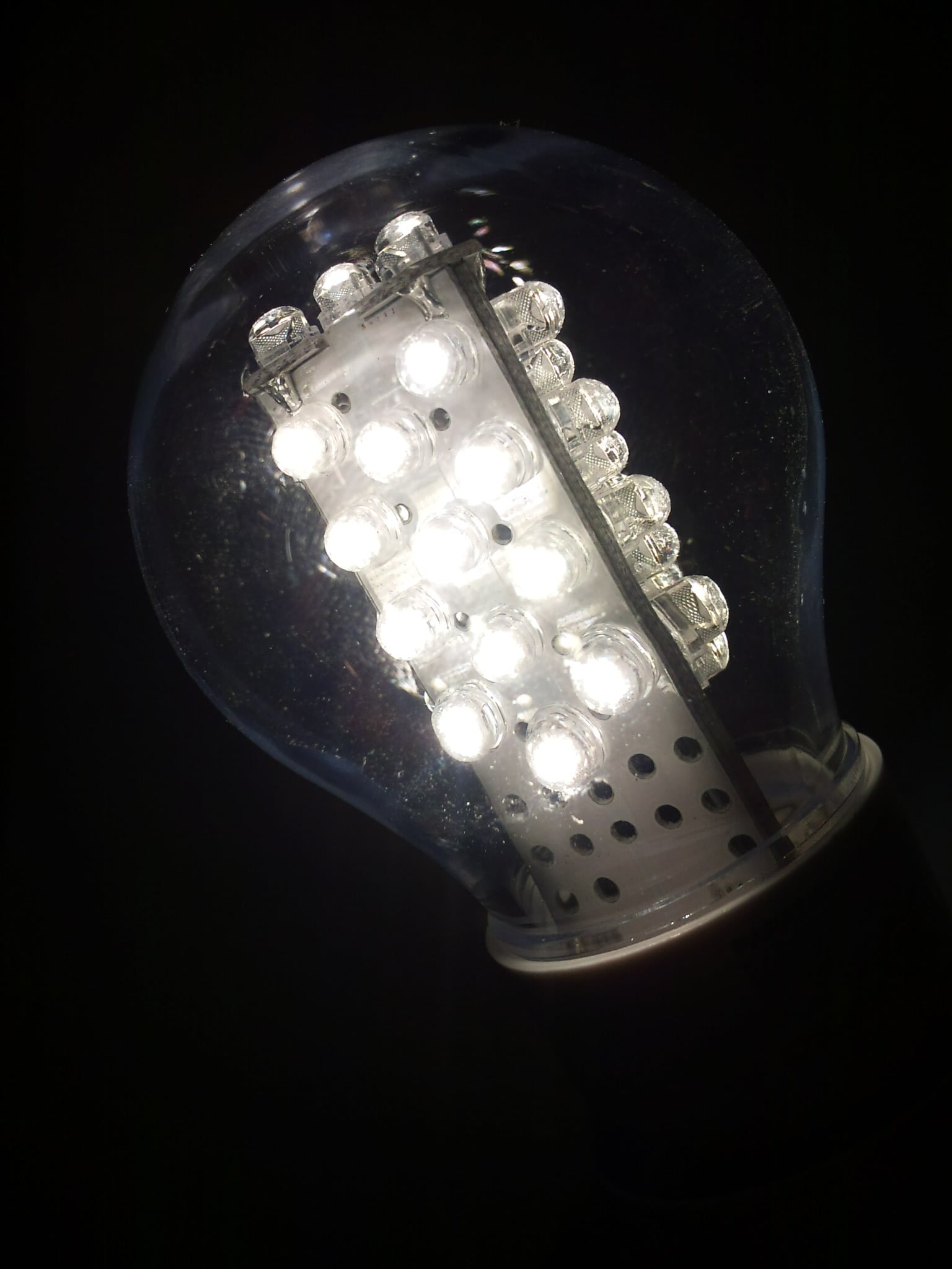 A close-up of a lit LED light bulb glowing brightly against a dark background, showing multiple small LED lights inside the transparent bulb.