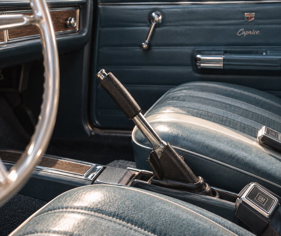 Close-up of a classic car’s blue interior, showing two front seats, a handbrake lever, part of the steering wheel, and door with a “Caprice” emblem.