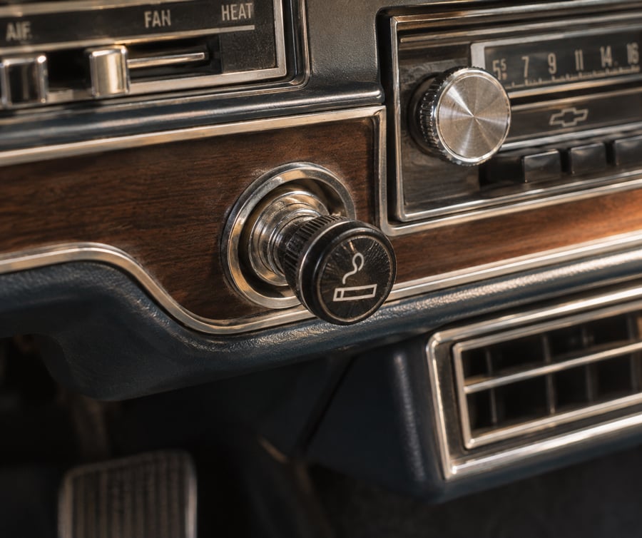 Close-up of a vintage car dashboard showing a cigarette lighter, air vent, radio, and control buttons with wood grain trim.
