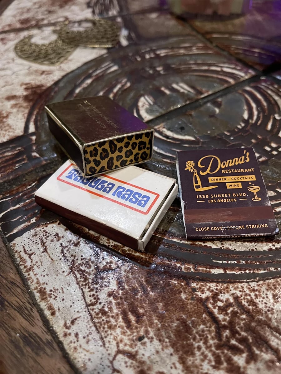 Three matchboxes rest on a rustic surface: one with a leopard print, one labeled “Casa Casa,” and one from Donna’s Restaurant on Sunset Blvd, Los Angeles.