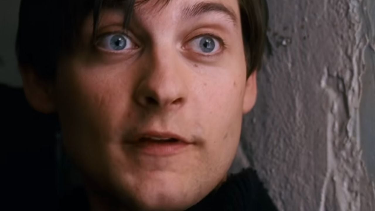 A close-up of a young person with blue eyes and dark hair, looking slightly to the side, standing near a textured wall.