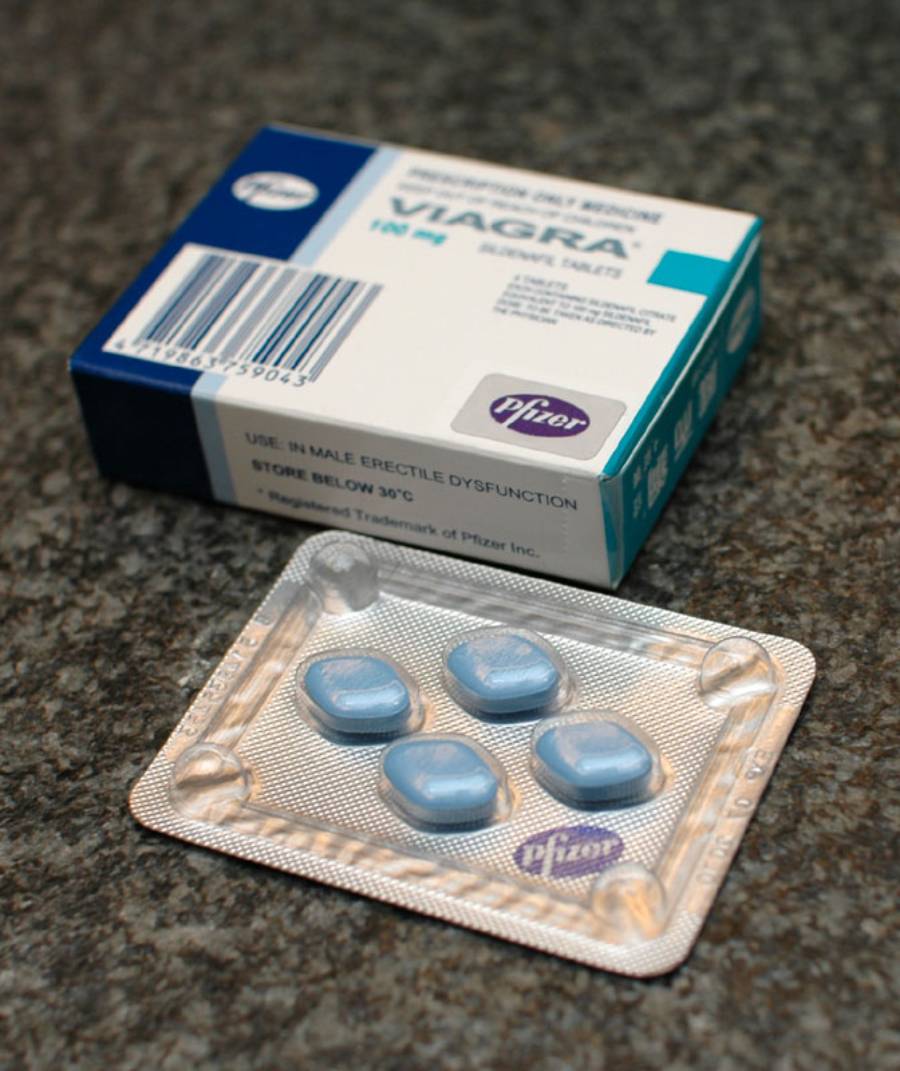 A blister pack of four blue, diamond-shaped Viagra pills in front of a blue and white Pfizer box on a textured surface.