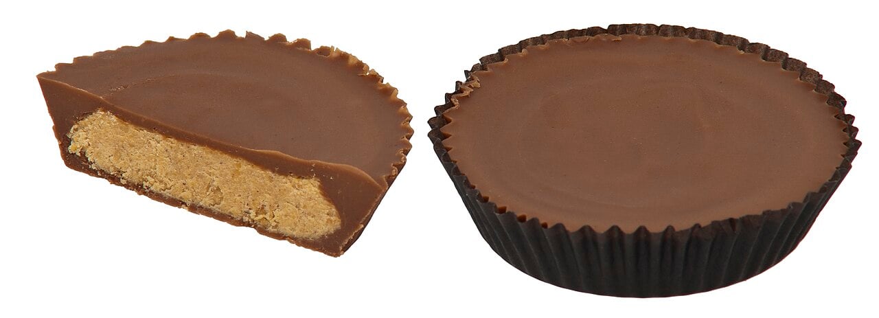 A whole chocolate peanut butter cup next to a half-cut cup showing the peanut butter filling.