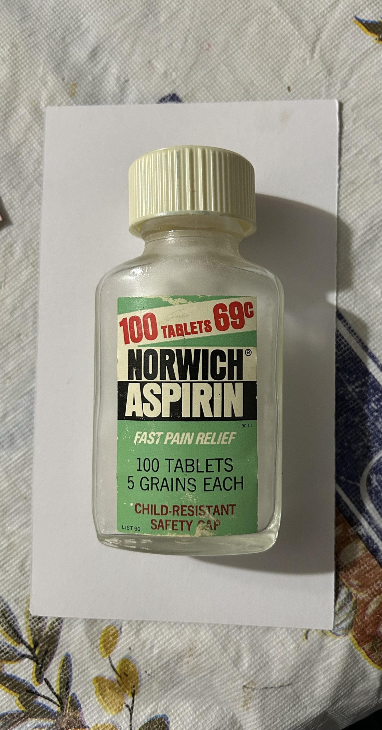 Small vintage glass bottle of Norwich Aspirin with a cream-colored child-resistant cap, labeled “100 tablets” and “5 grains each.”